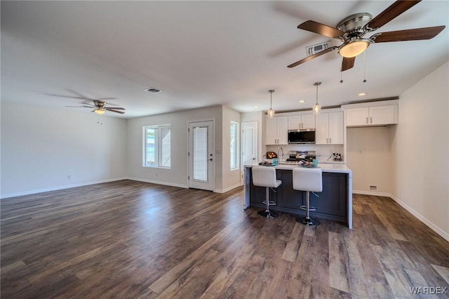 kitchen with a center island with sink, stainless steel microwave, dark wood-style floors, white cabinets, and baseboards