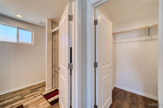 bathroom with a walk in closet, wood finished floors, and baseboards