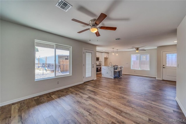 unfurnished living room with dark wood-type flooring, baseboards, visible vents, and a sink