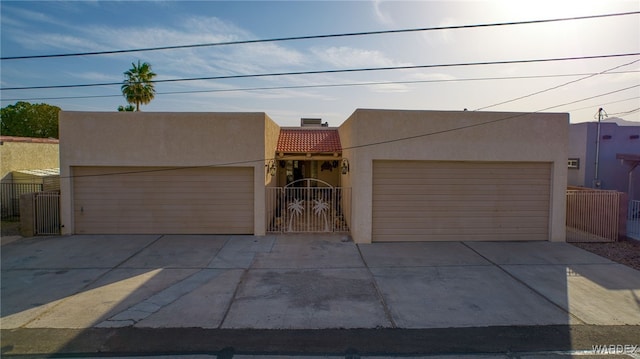 pueblo revival-style home featuring an attached garage, a tile roof, a gate, and stucco siding