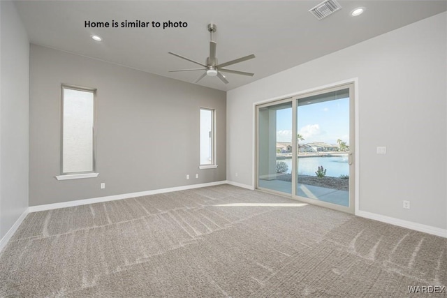 empty room with a water view, baseboards, visible vents, and light colored carpet