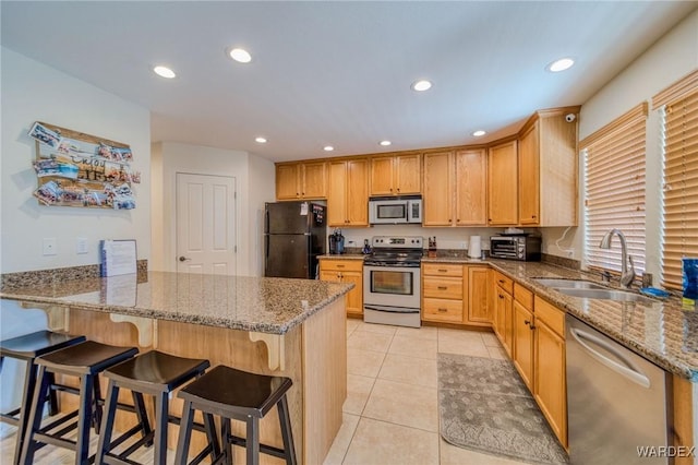 kitchen with a breakfast bar area, stone countertops, stainless steel appliances, a peninsula, and a sink