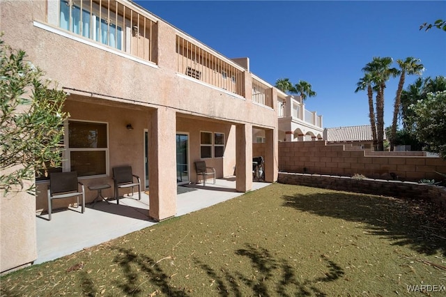 back of property with stucco siding, fence, a lawn, and a patio