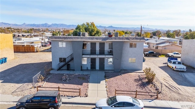 view of front facade with a balcony, fence, a mountain view, and stucco siding