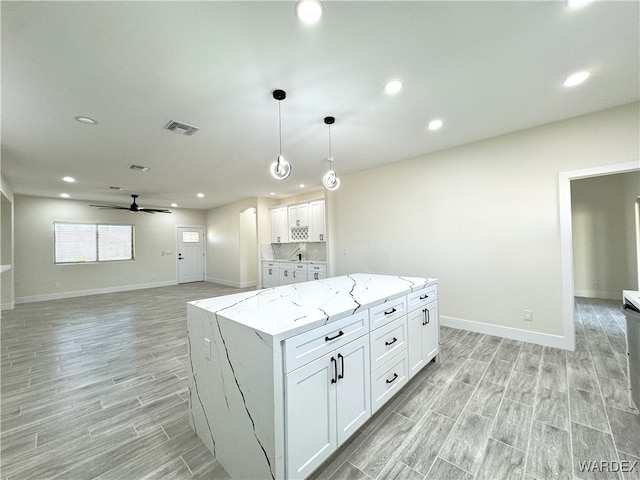 kitchen with light stone counters, visible vents, white cabinetry, a center island, and pendant lighting