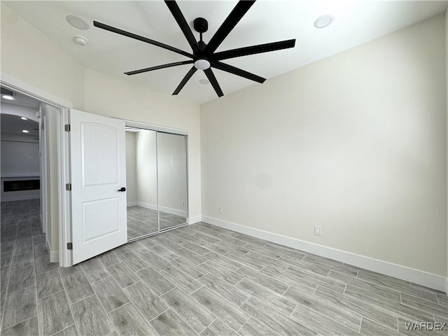 unfurnished bedroom featuring wood tiled floor, baseboards, ceiling fan, and a closet