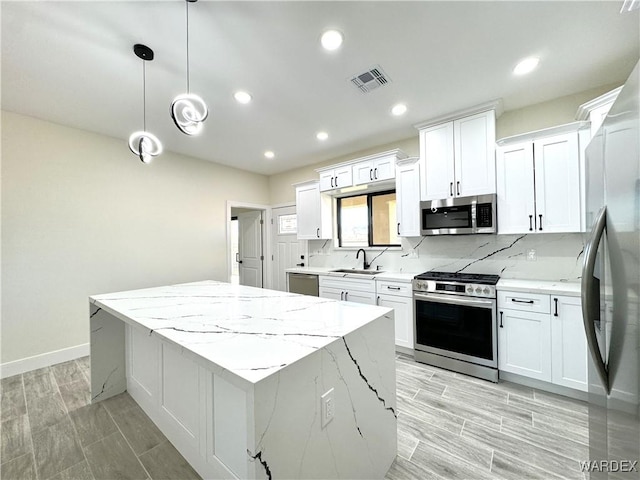 kitchen featuring stainless steel appliances, white cabinetry, hanging light fixtures, and a sink