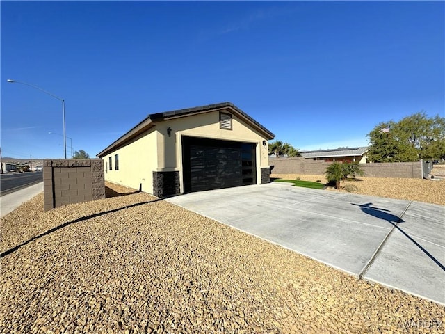 view of side of home with an outbuilding, a garage, fence, concrete driveway, and stucco siding