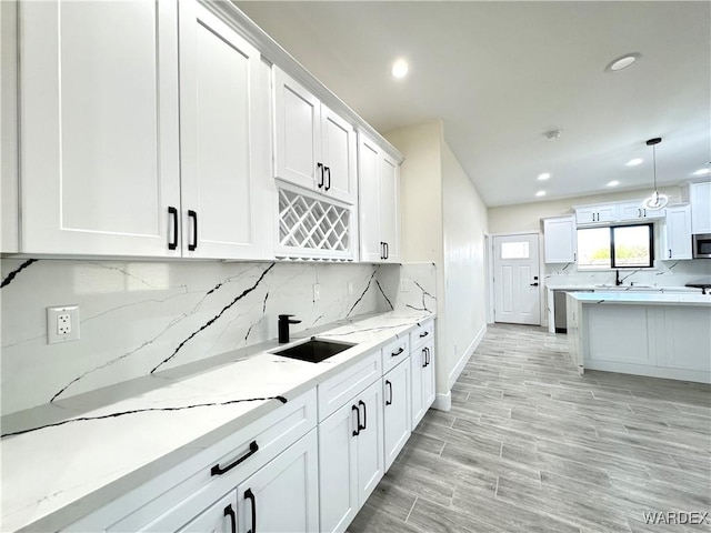 kitchen with light stone counters, tasteful backsplash, hanging light fixtures, white cabinetry, and a sink