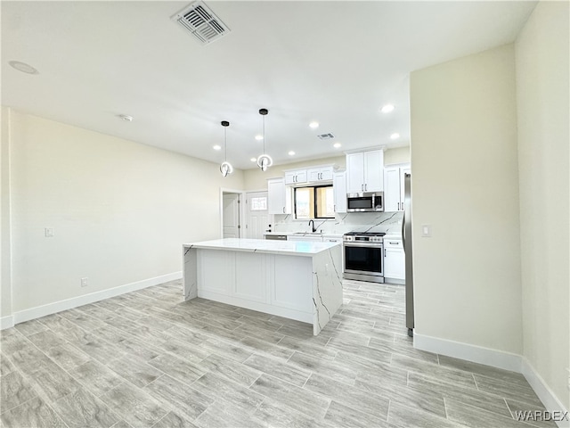 kitchen with light countertops, visible vents, appliances with stainless steel finishes, white cabinetry, and a kitchen island