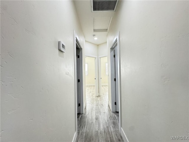 corridor with attic access, visible vents, baseboards, and wood finished floors