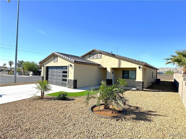 view of front of house with concrete driveway, stone siding, an attached garage, fence, and stucco siding