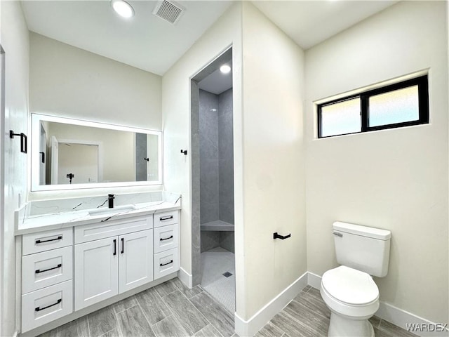 bathroom featuring a walk in shower, toilet, vanity, visible vents, and baseboards