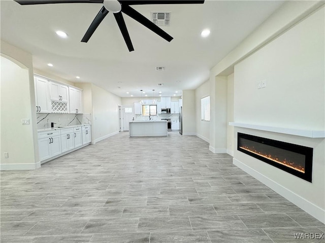 unfurnished living room with a ceiling fan, a glass covered fireplace, baseboards, and recessed lighting