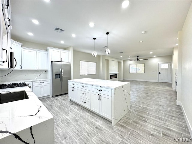 kitchen with white cabinets, a kitchen island, appliances with stainless steel finishes, open floor plan, and hanging light fixtures