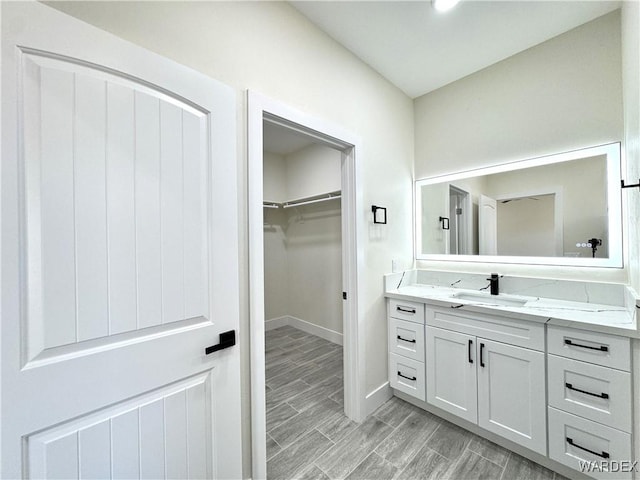 bathroom with wood finish floors, baseboards, a spacious closet, and vanity