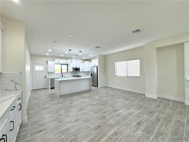 kitchen featuring decorative light fixtures, stainless steel appliances, visible vents, white cabinetry, and a kitchen island