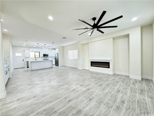 unfurnished living room with light wood-type flooring, a glass covered fireplace, a wealth of natural light, and recessed lighting