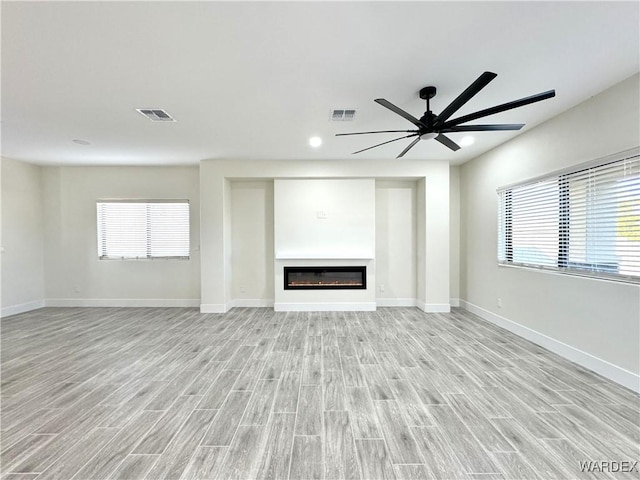 unfurnished living room featuring light wood-style floors, baseboards, visible vents, and a glass covered fireplace