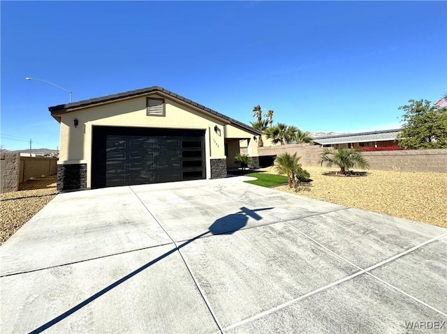 single story home featuring a garage, fence, stone siding, concrete driveway, and stucco siding