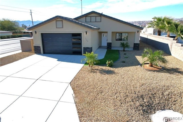 view of front of property with stucco siding, fence, a garage, stone siding, and driveway