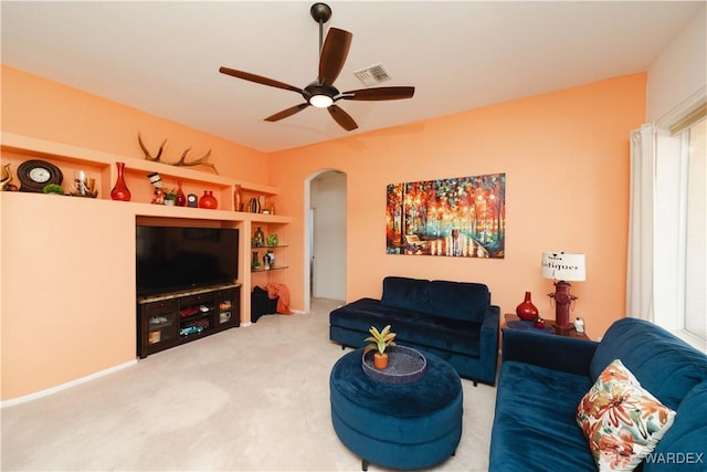 living area with a ceiling fan, arched walkways, visible vents, and carpet