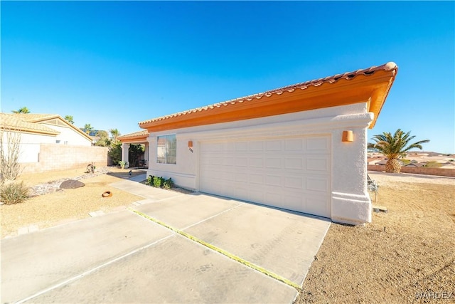 view of front of home with concrete driveway, a tile roof, fence, and stucco siding