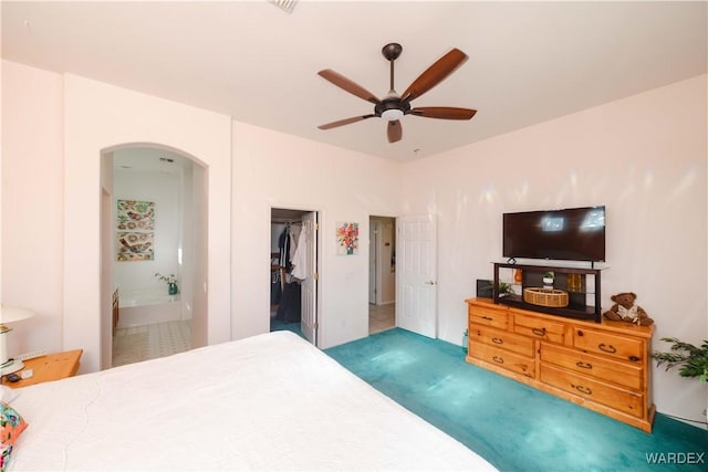 bedroom with arched walkways, ceiling fan, ensuite bathroom, a spacious closet, and dark colored carpet