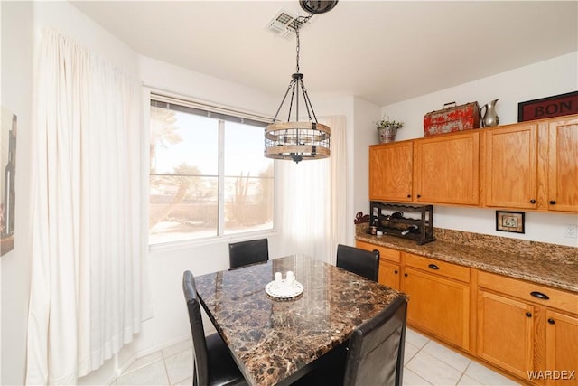 kitchen with light tile patterned floors, visible vents, a kitchen island, brown cabinets, and dark stone countertops