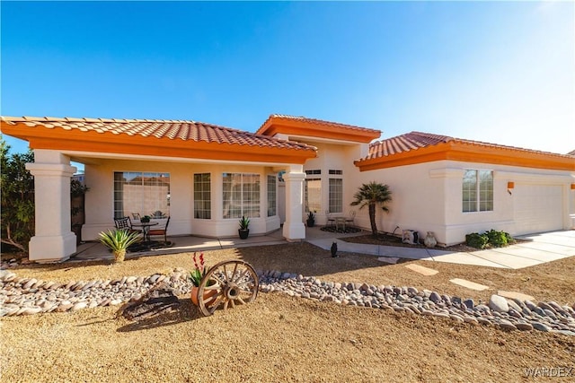 rear view of property featuring an attached garage, a tile roof, and stucco siding