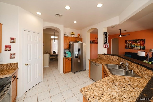 kitchen featuring arched walkways, brown cabinets, stainless steel appliances, visible vents, and a sink