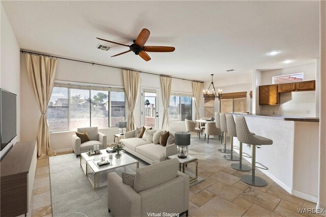 living room featuring stone tile flooring, visible vents, baseboards, and ceiling fan with notable chandelier