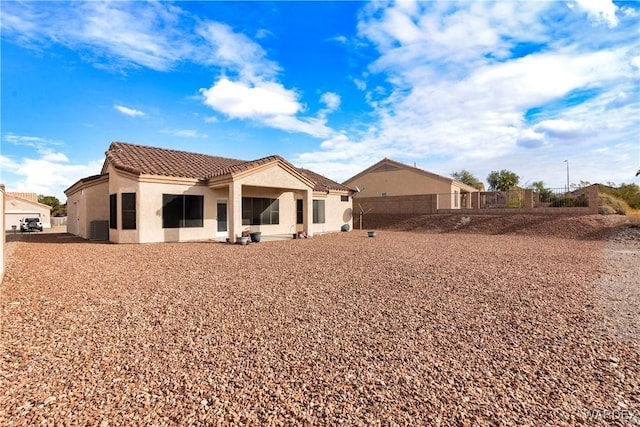 back of house featuring fence, a tiled roof, and stucco siding