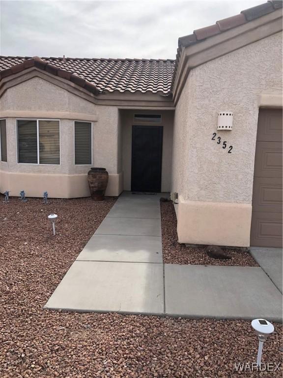 doorway to property featuring an attached garage, a tile roof, and stucco siding