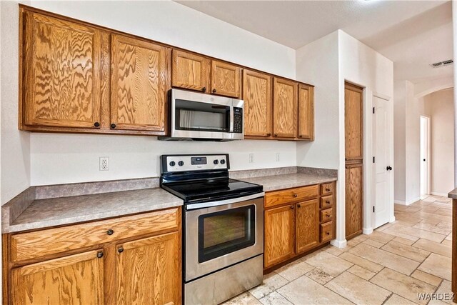 kitchen featuring arched walkways, light countertops, visible vents, appliances with stainless steel finishes, and brown cabinetry