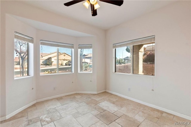 empty room featuring a ceiling fan, stone tile flooring, plenty of natural light, and baseboards