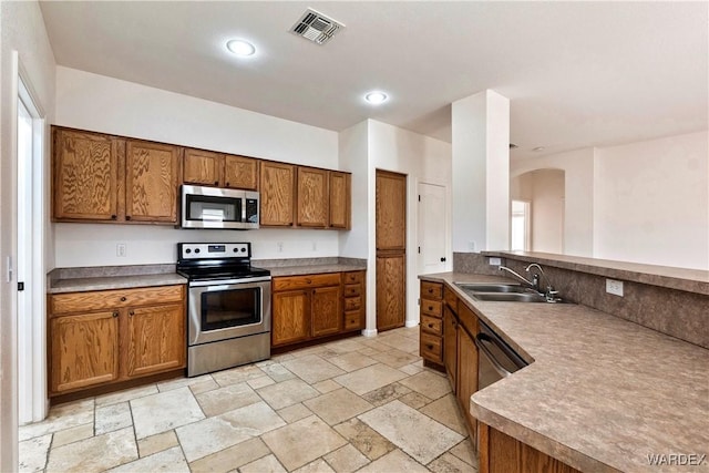 kitchen featuring brown cabinetry, visible vents, stainless steel appliances, and a sink