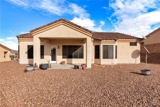 back of house featuring a tile roof, a patio area, and stucco siding