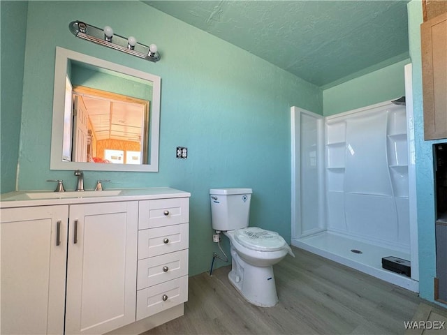 bathroom with vanity, a stall shower, a textured ceiling, toilet, and wood finished floors