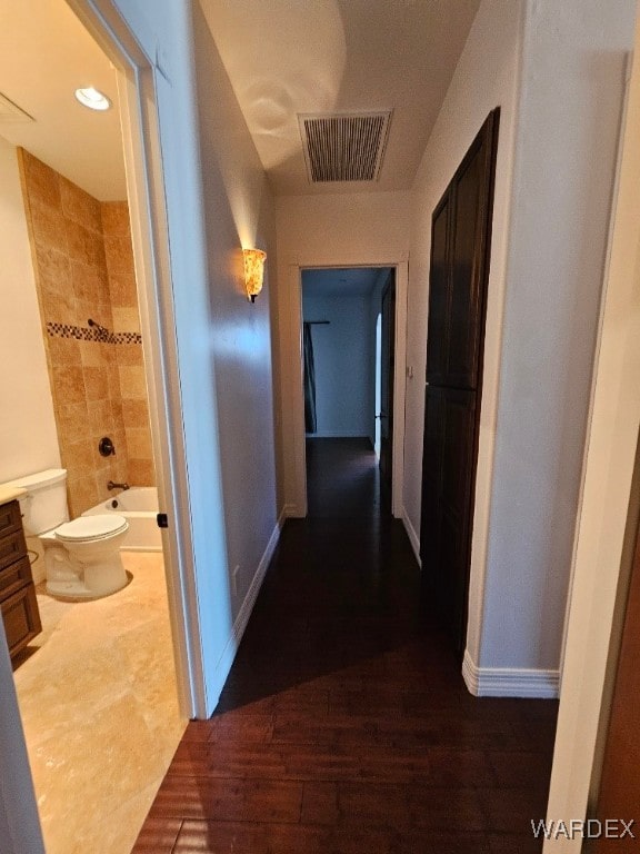 corridor featuring dark wood-style floors, visible vents, and baseboards