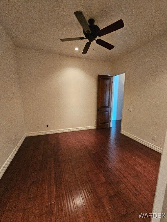 unfurnished room featuring ceiling fan, dark wood finished floors, and baseboards