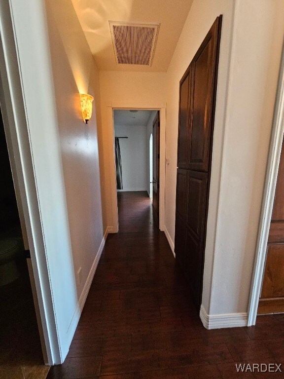 corridor with dark wood-style floors, visible vents, and baseboards