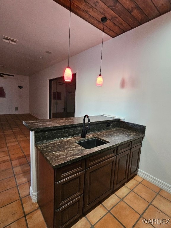 kitchen featuring dark brown cabinetry, visible vents, a peninsula, pendant lighting, and a sink