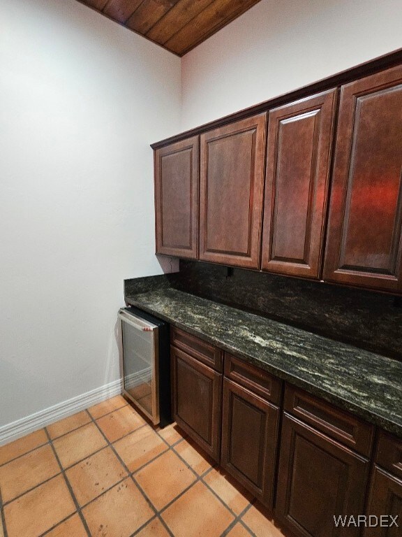 kitchen featuring baseboards, light tile patterned flooring, dark brown cabinets, and dark stone countertops