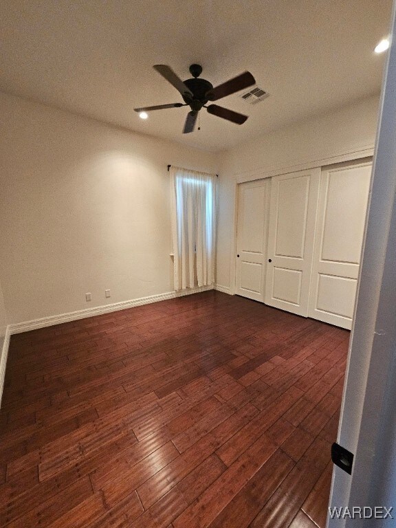 unfurnished bedroom featuring baseboards, visible vents, a ceiling fan, dark wood-style floors, and a closet