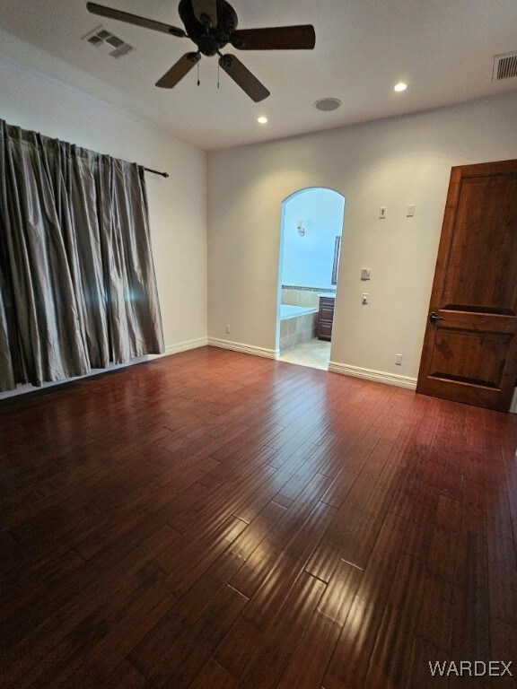 unfurnished room featuring dark wood-style floors, baseboards, visible vents, and arched walkways