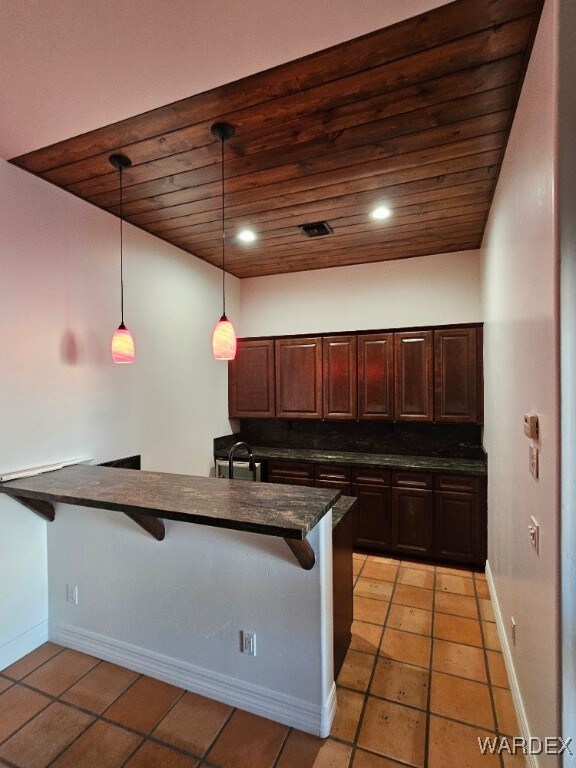 kitchen featuring a peninsula, dark countertops, a kitchen bar, and decorative light fixtures