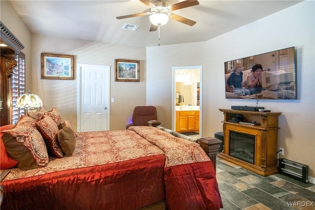 bedroom featuring a ceiling fan, a glass covered fireplace, visible vents, and connected bathroom