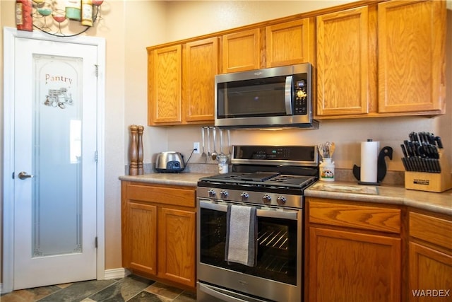 kitchen featuring light countertops, appliances with stainless steel finishes, stone finish flooring, and brown cabinets