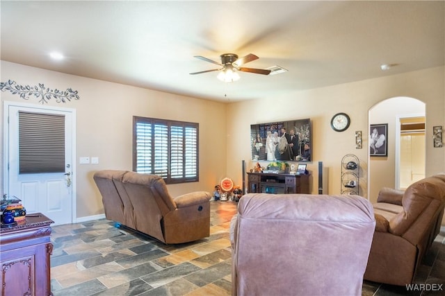 living room featuring arched walkways, visible vents, stone finish floor, and a ceiling fan